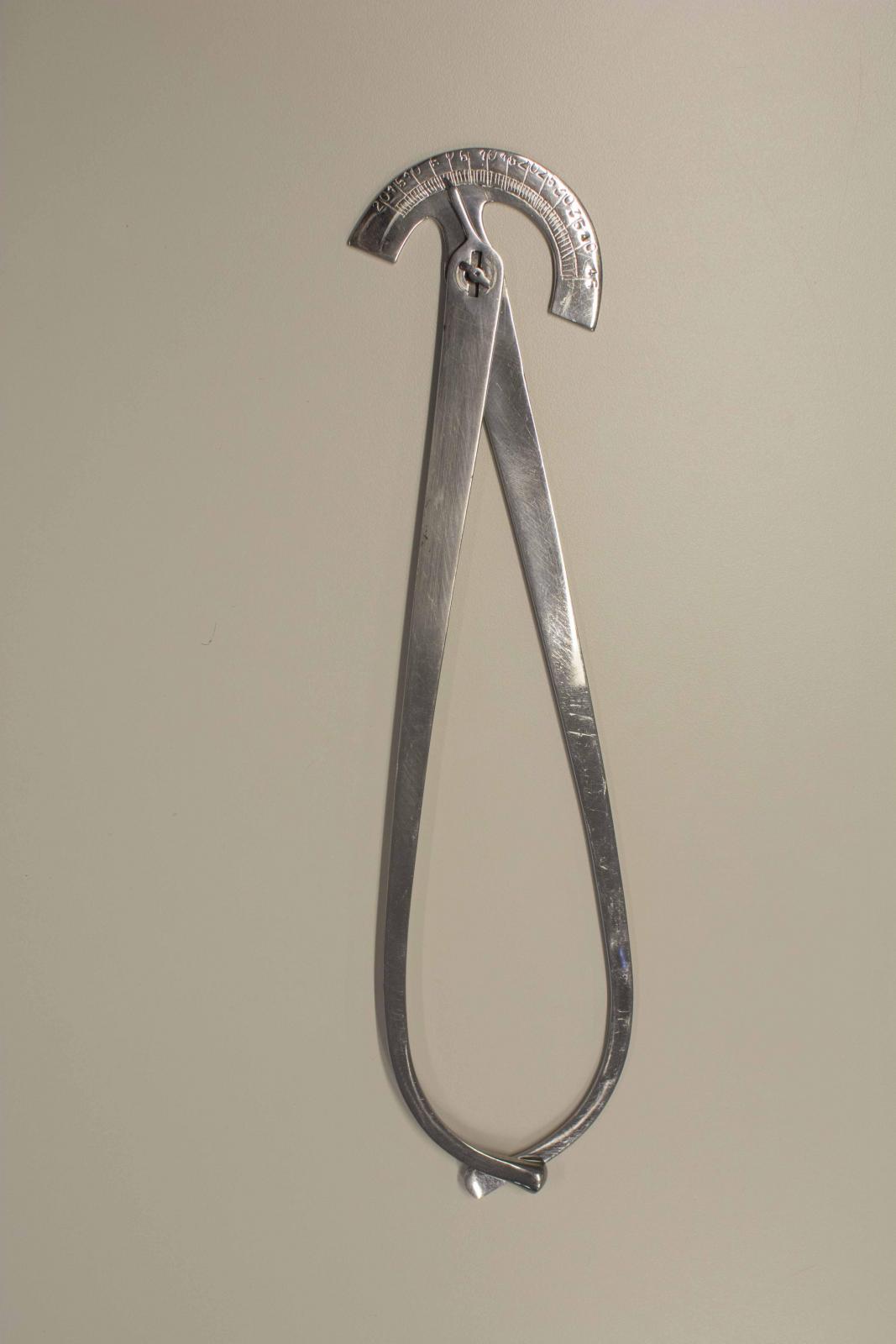 Instrumento metálico formado por dos piezas alargadas que en un extremo terminan en curva y en el contrario cuentan con una aguja y un semicírculo de medida de ángulos, respectivamente. Quedan unidos en este extremo con mediante un tornillo que facilita su movilidad.