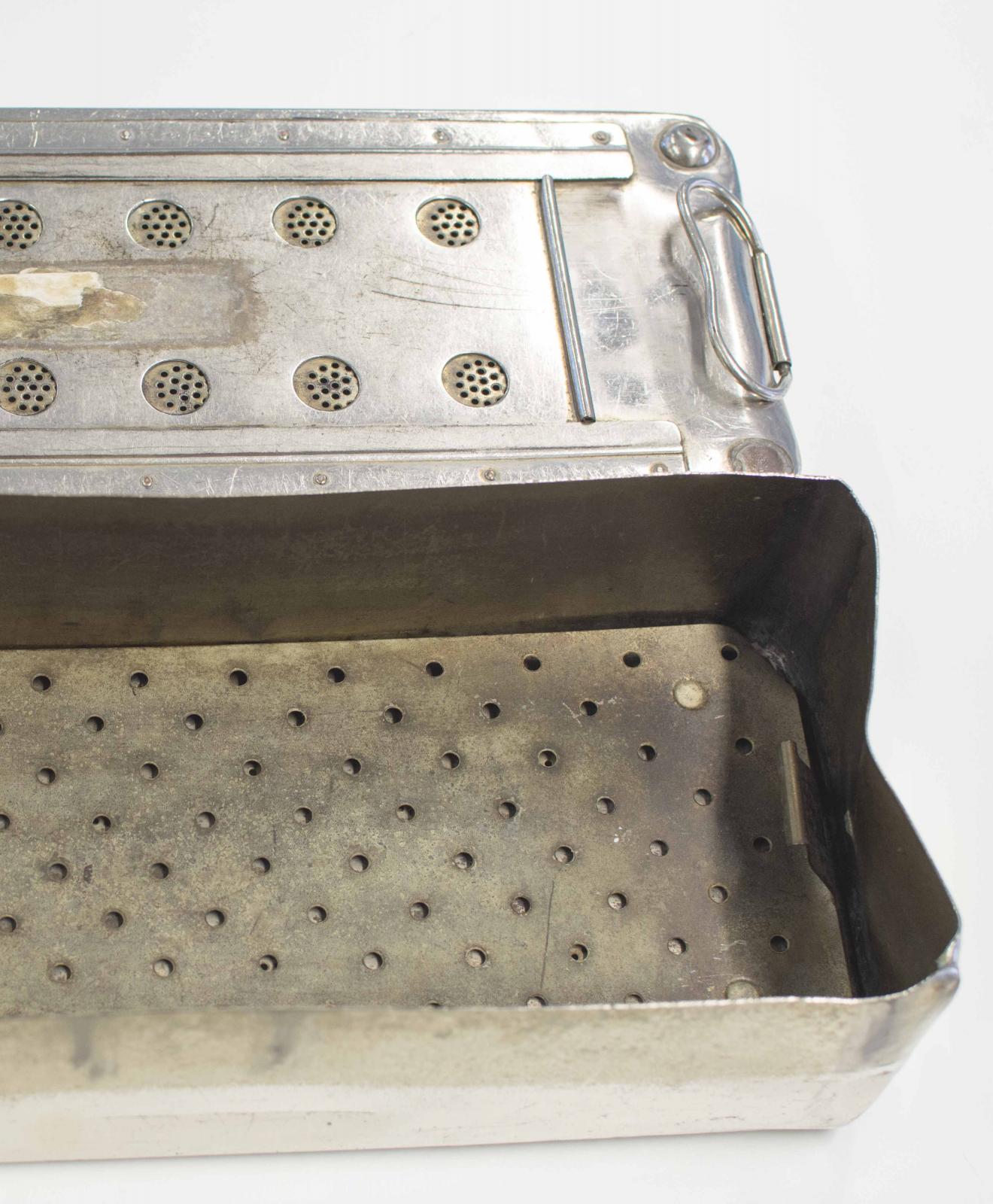 Caja metálica con rejilla en su interior. Tapadera con círculos perforados para ventilación y asas laterales