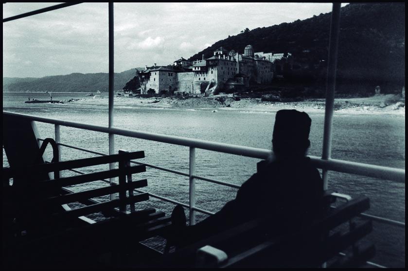 Monje en la barcaza de transporte, al fondo, Monasterio de Xenophontos. Monte Athos