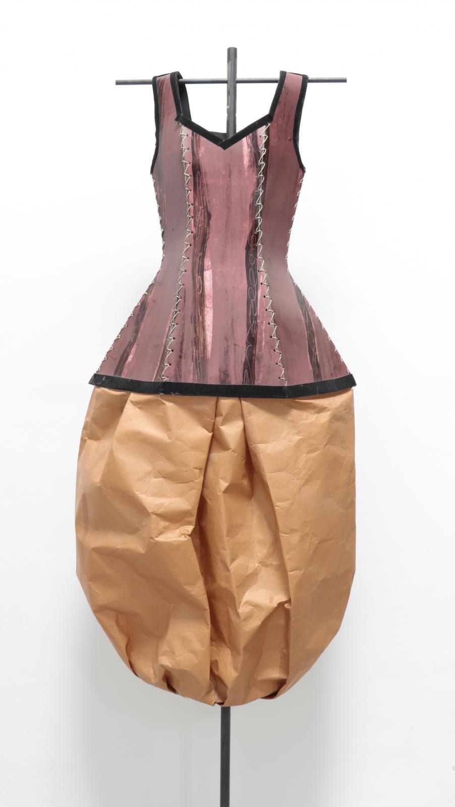 Vestido escultura compuesto por corpiño rosa envejecido de material rígido cosido en secciones verticales, bajo el que se abre una falda globo de papel marrón